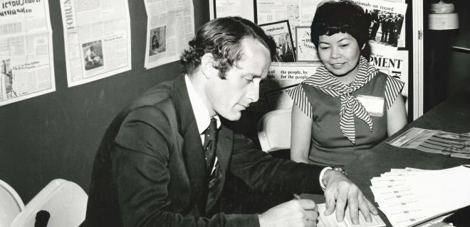 A male is writing and sitting beside a female